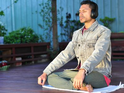 Person taking a deep breath outdoors with eyes closed.